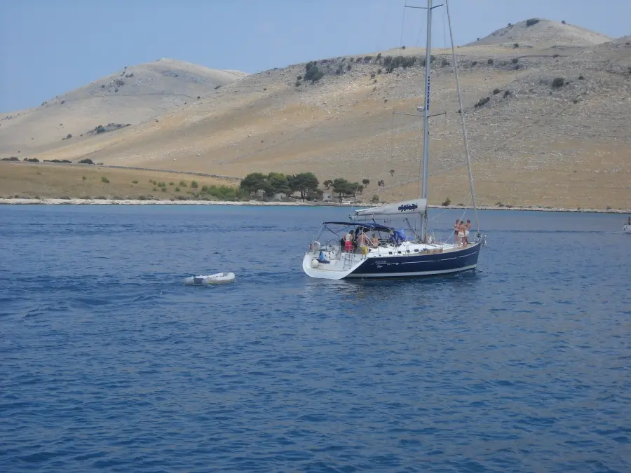 Ein Segelboot vor Anker in den ruhigen Gewässern vor der Insel Murter, im Hintergrund ein schroffer, karger Hügel unter einem klaren blauen Himmel