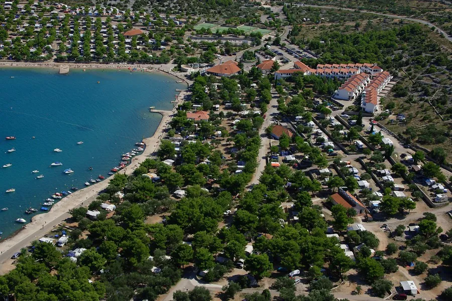 Aerial view of a residential area with houses and pools next to a body of water.