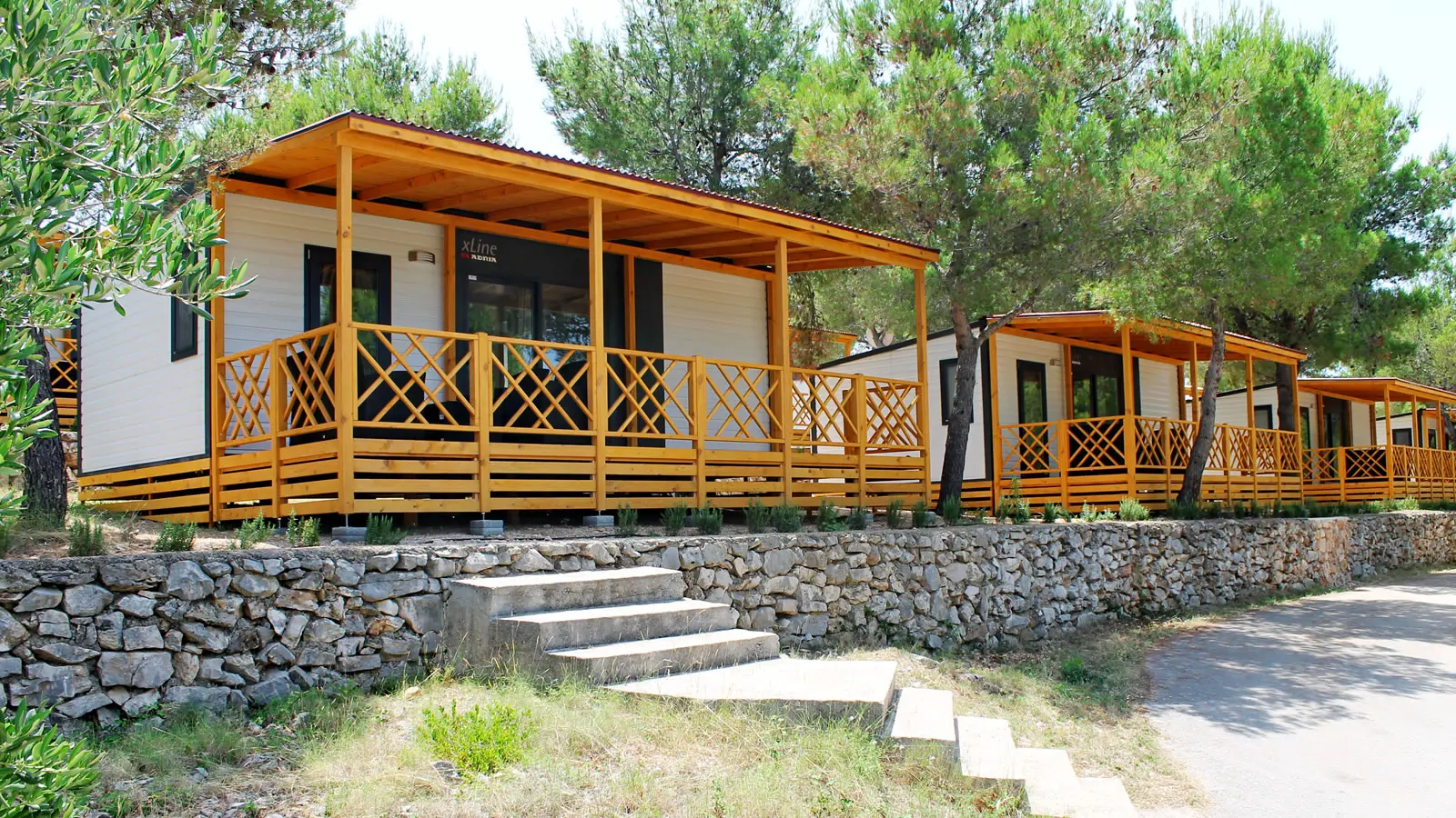 Row of modern mobile homes with yellow wooden porches surrounded by pine trees at a resort in Jezera, Murter