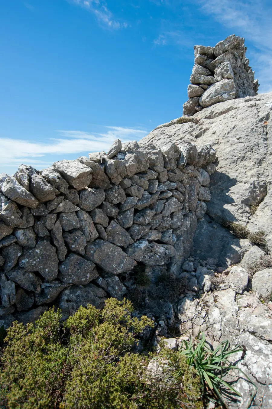 Eine traditionelle Trockenmauer vor einem Felsvorsprung unter einem klaren blauen Himmel, die die raue Naturlandschaft der Insel Murter zeigt