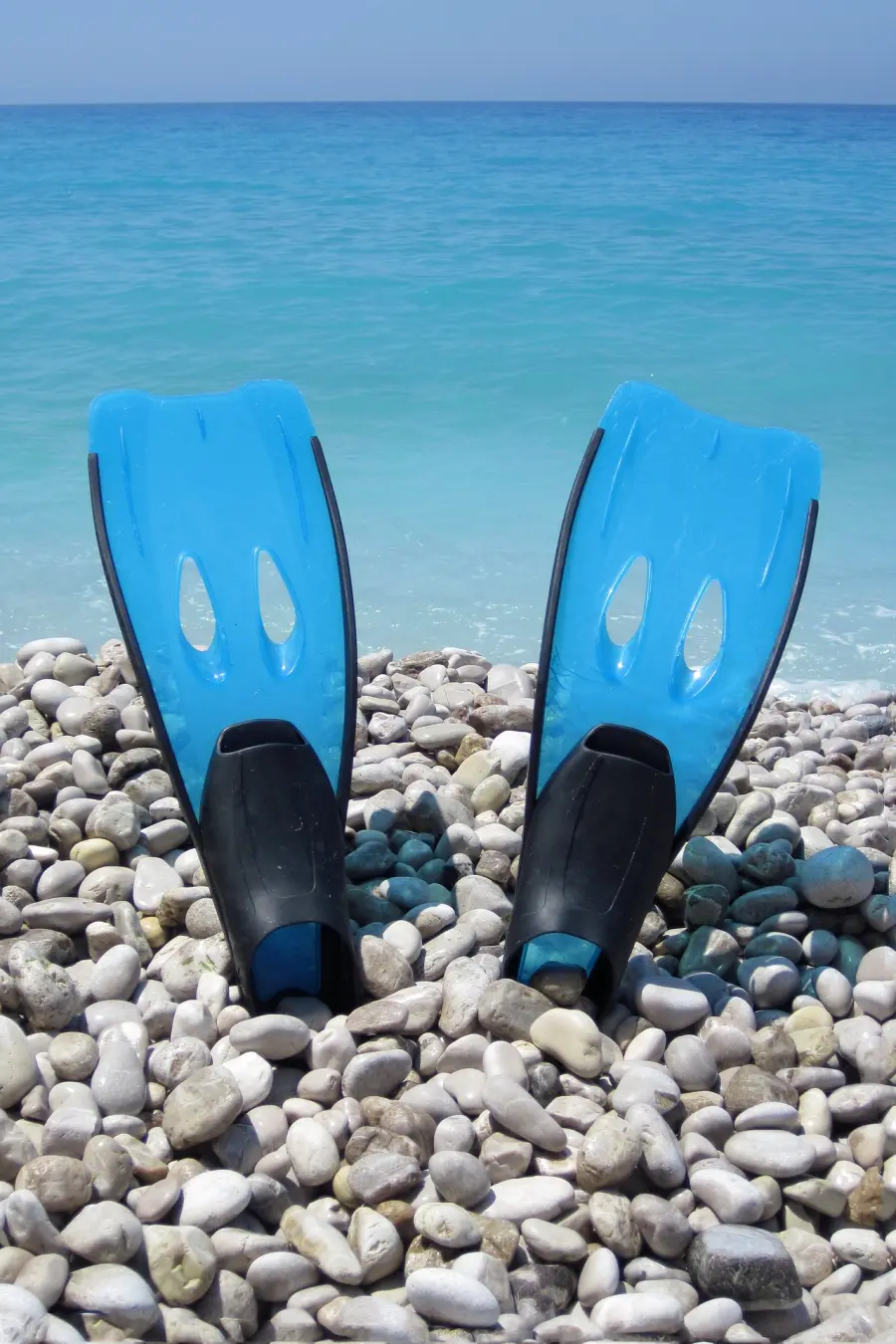 Blaue Schwimmflossen an einem Kiesstrand mit dem türkisfarbenen Meer im Hintergrund, bereit für ein Schnorchelabenteuer im klaren Wasser der Insel Murter.