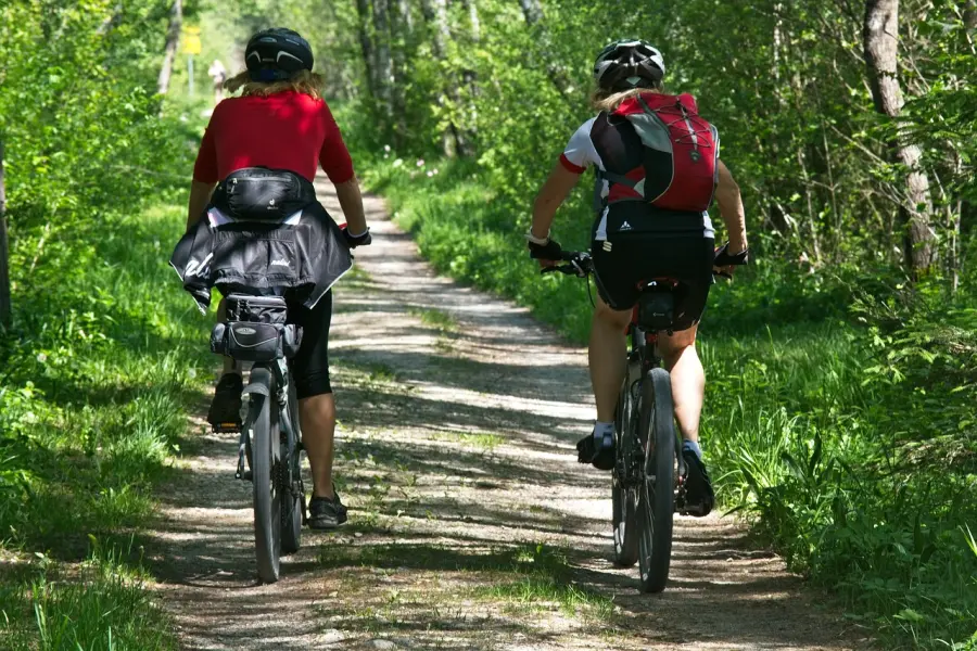 Dvije osobe voze bicikle zemljanom cestom.