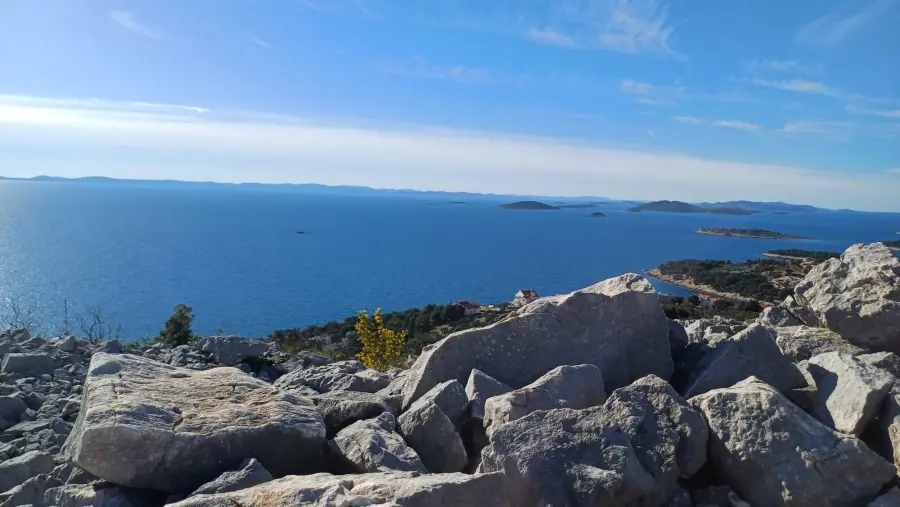 Pogled sa stjenovitog brežuljka koji gleda na prostrano Jadransko more s raštrkanim otocima i obalu otoka Murtera u daljini.