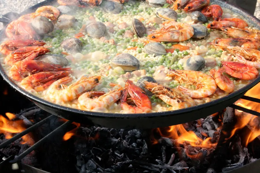 Brutzelnde Paella mit Meeresfrüchten, die auf offener Flamme mit Garnelen, Muscheln und Erbsen in einer großen traditionellen Pfanne zubereitet wird und die mediterrane Küche verkörpert