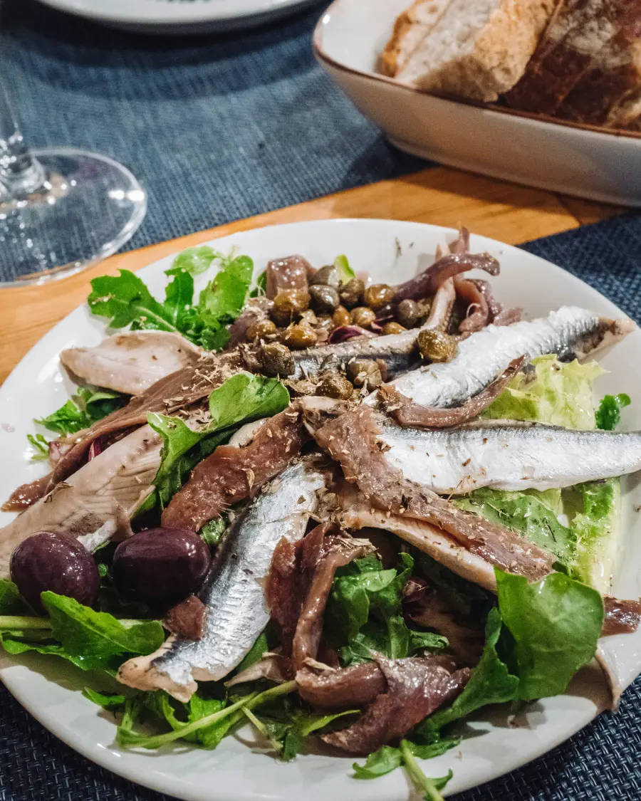 Svježa mediteranska salata s inćunima, maslinama i miješanim zelenim salatama na bijelom tanjuru, popraćena hrskavim kruhom