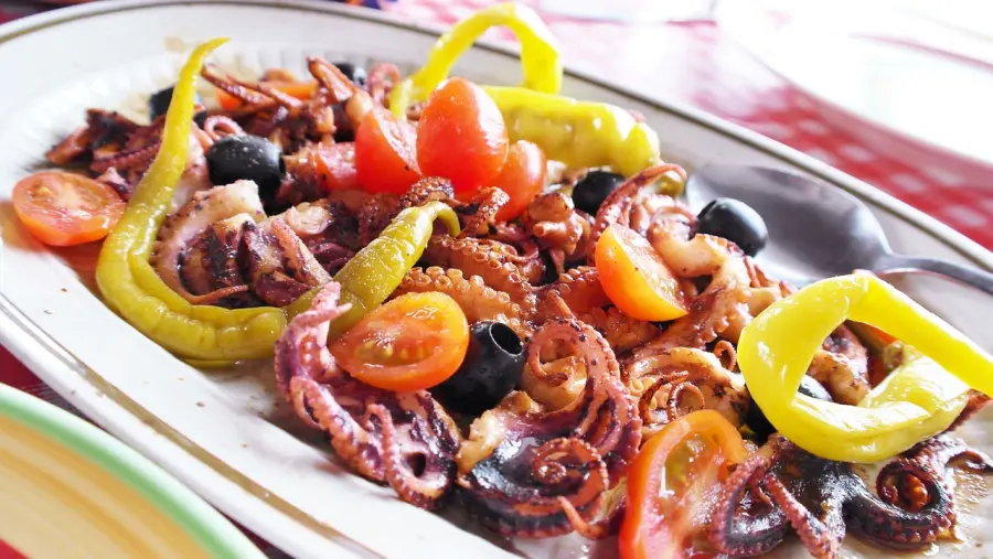 Salata od hobotnice sa svježim rajčicama, maslinama i papričicama, servirana na tanjuru, tradicionalno mediteransko jelo.