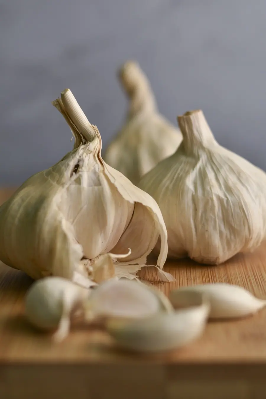 Fresh garlic bulbs with cloves partially peeled, resting on a wooden chopping board, showcasing essential ingredients in culinary preparation