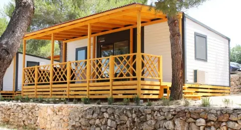 Pogled izvana na modernu mobilnu kućicu sa žarko žutim trijemom smještenu pod borovima u turističkom naselju Jezera na Murteru