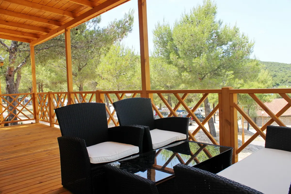 Comfortable patio furniture on the deck of a camping mobile home, shaded by pine trees with a view of the Jezera landscape.