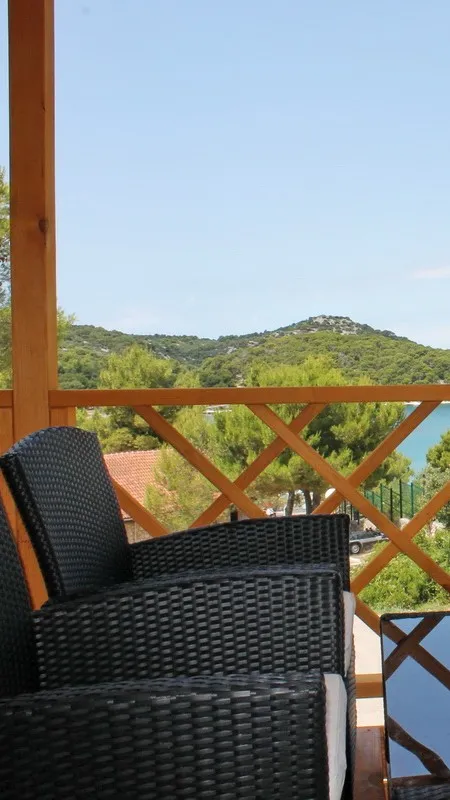Entspannender Terrassenblick von einem Mobilheim mit Korbstühlen, die auf die üppigen Hügel und das ruhige Wasser der Insel Murter blicken.