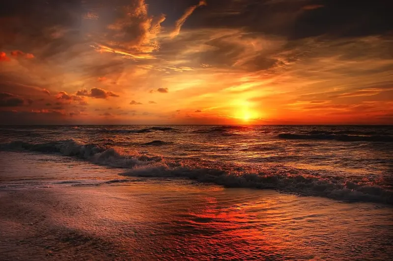 Dramatičen sončni zahod nad mirnim morjem, nebo v ognjenih odtenkih oranžne in rdeče barve.
