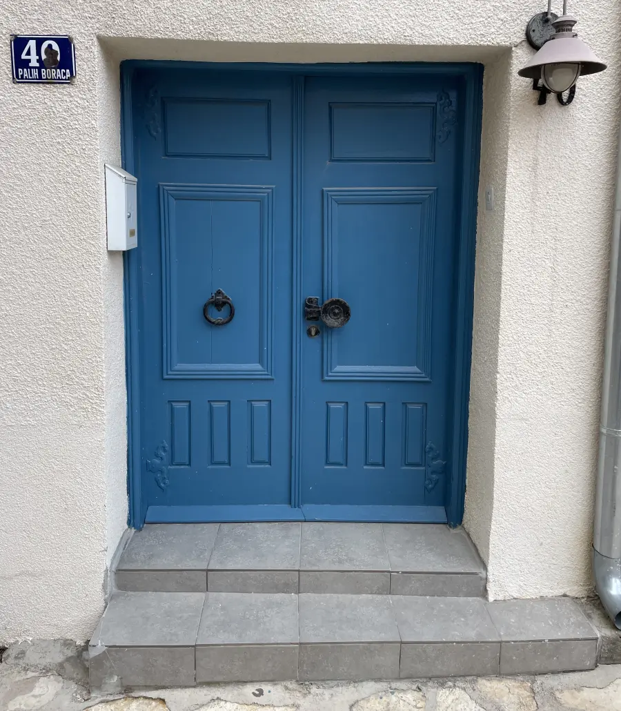 Blue door on white building  with black handles. Text on the building says "40 PALIH BORACA"