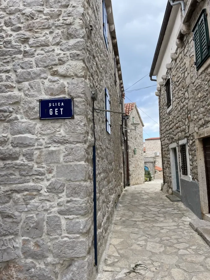Narrow street in an old town. There is a blue sign with white text that says "ULICA GET" on the wall.